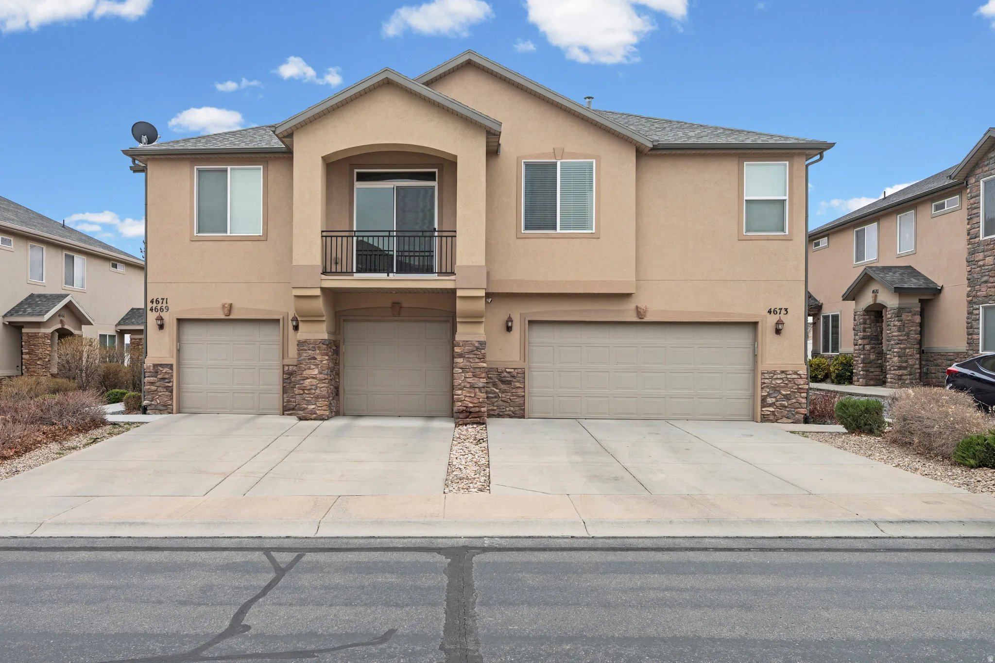 View of front of property featuring a balcony, stucco siding, stone siding, and a garage
