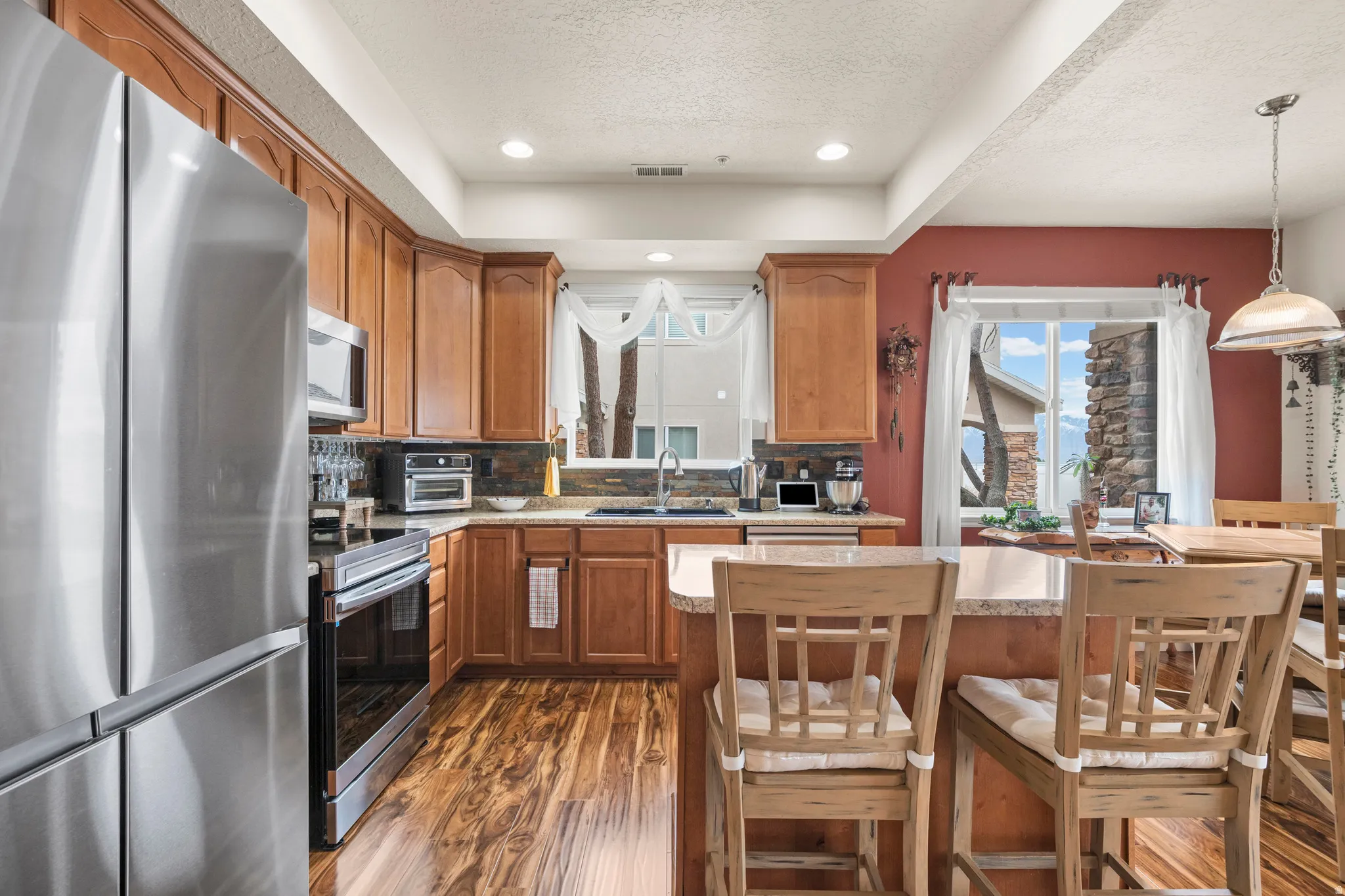Kitchen with stainless steel appliances, wood finish cabinetry, dark wood-style floors, backsplash, and a textured ceiling