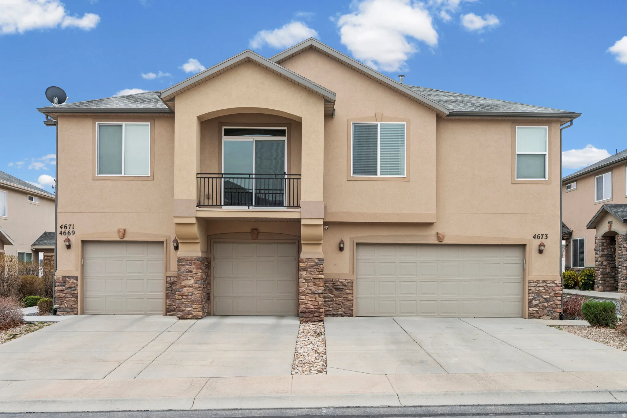 View of front of house featuring a balcony, stucco siding, a garage, and stone siding