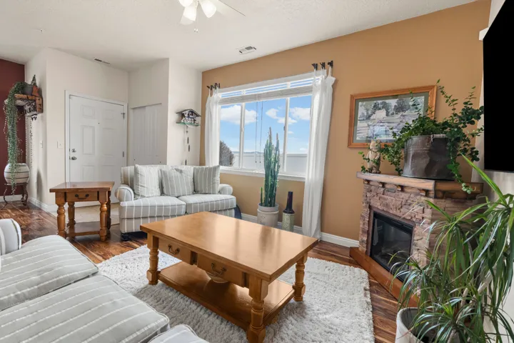 Living room with a stone fireplace, a ceiling fan, wood finished floors, and a textured ceiling