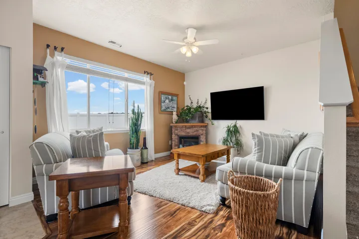 Living area with ceiling fan, a stone fireplace, a textured ceiling, and wood finished floors