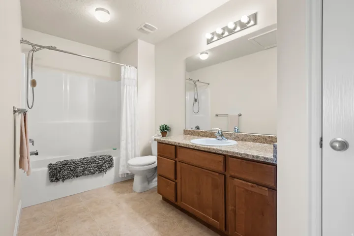 Bathroom with vanity, a textured ceiling, shower / bath combination with curtain, and light tile patterned flooring