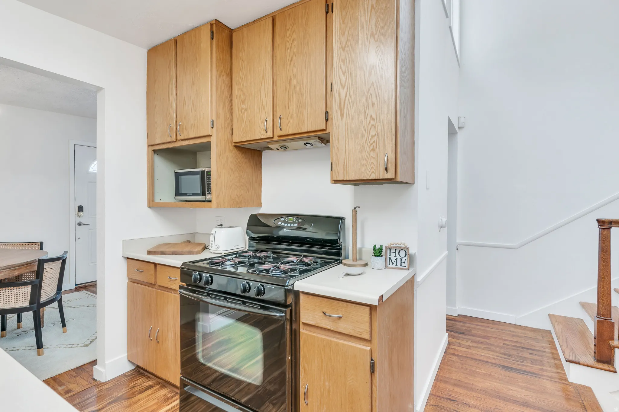 Kitchen with black gas range oven, light countertops, stainless steel microwave, and light wood-style flooring