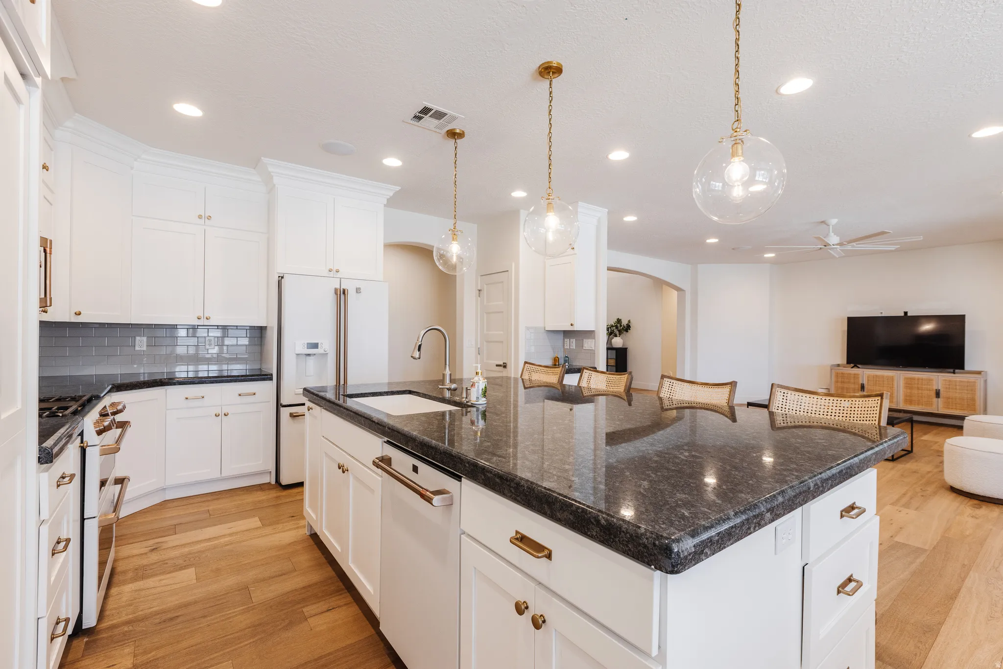 Kitchen with a large island, open floor plan, light wood-style flooring, arched walkways, and white appliances