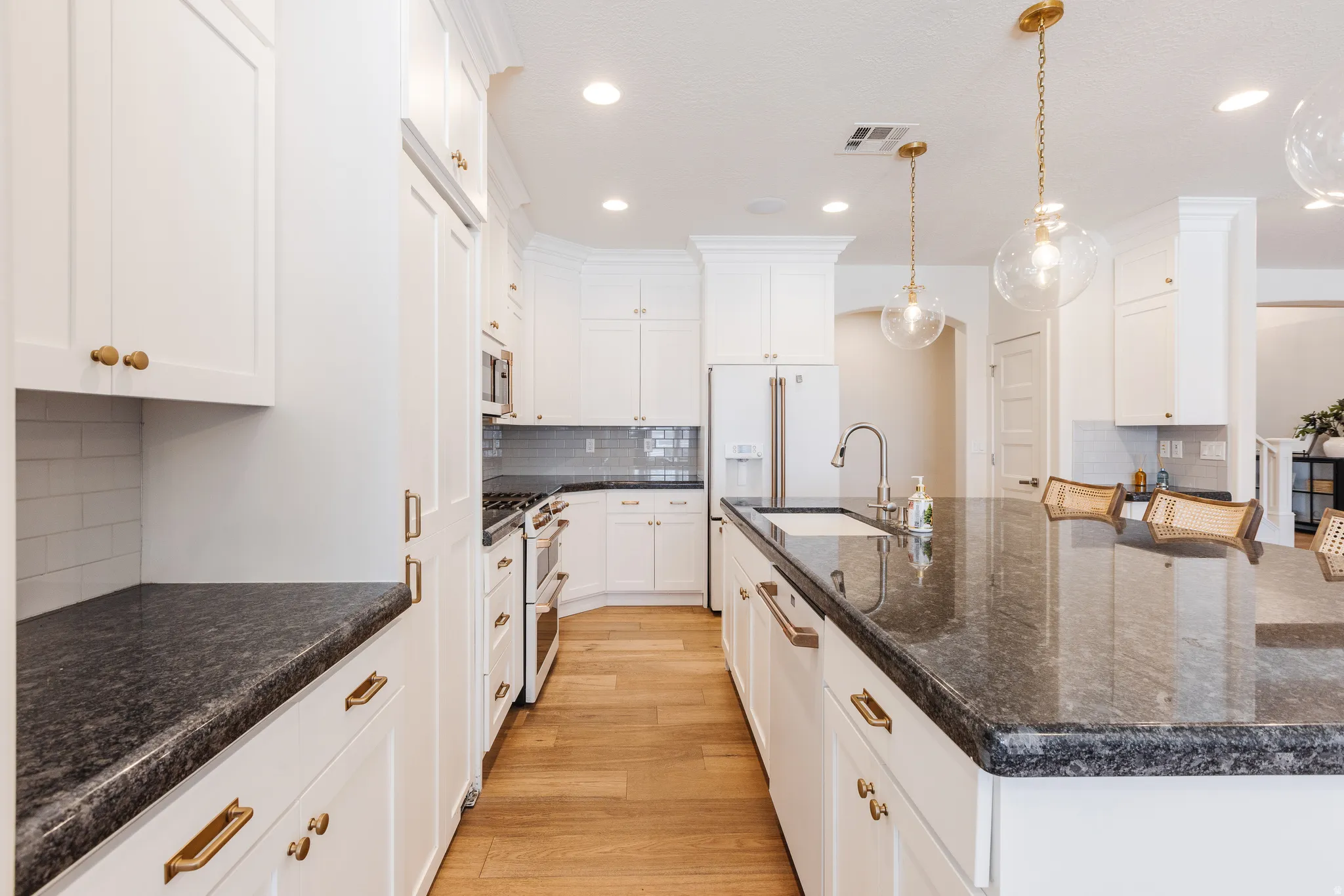 Kitchen featuring decorative backsplash, a large island with sink, light wood finished floors, high quality appliances, and white cabinetry