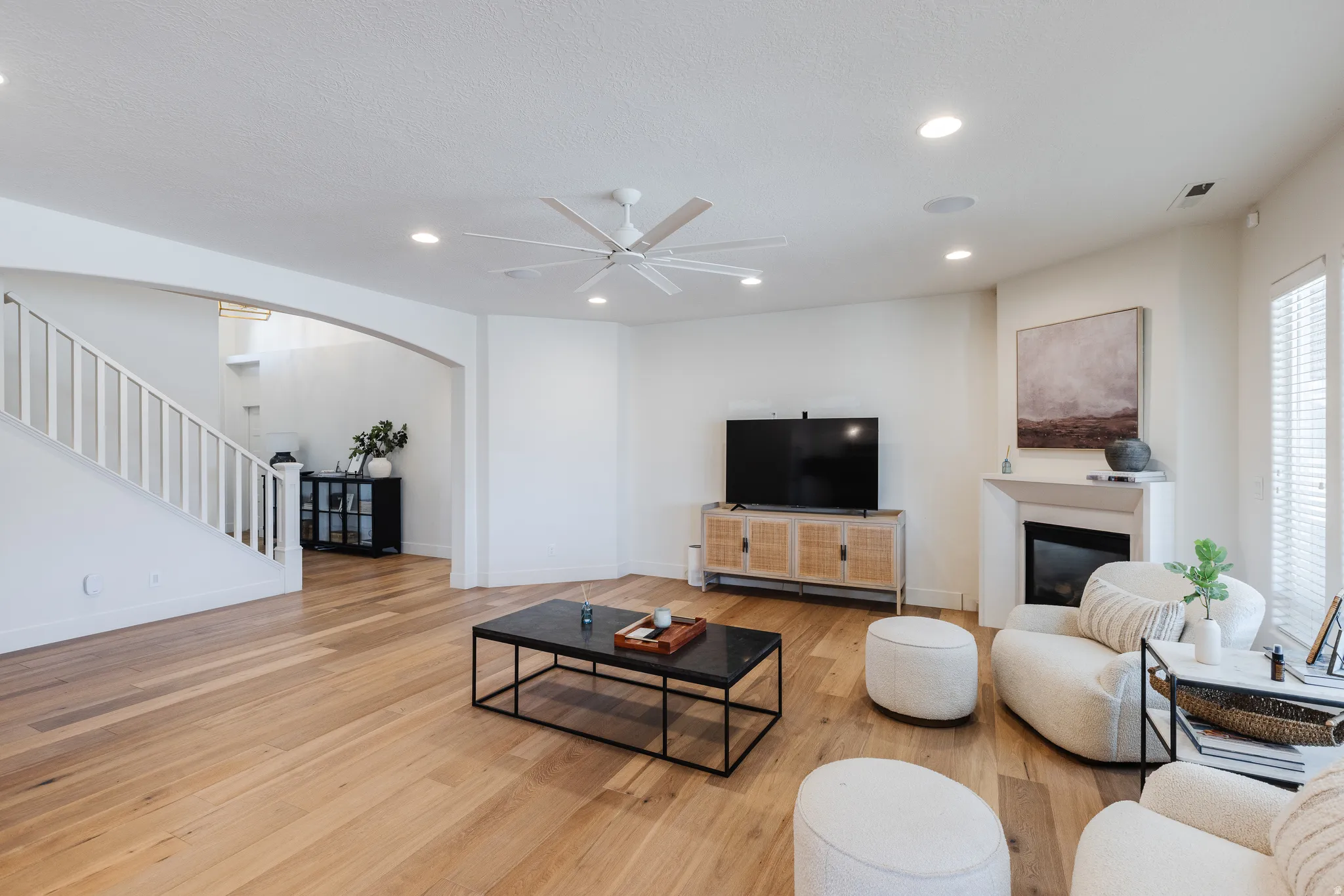 Living room with a ceiling fan, arched walkways, light wood finished floors, recessed lighting, and a glass covered fireplace