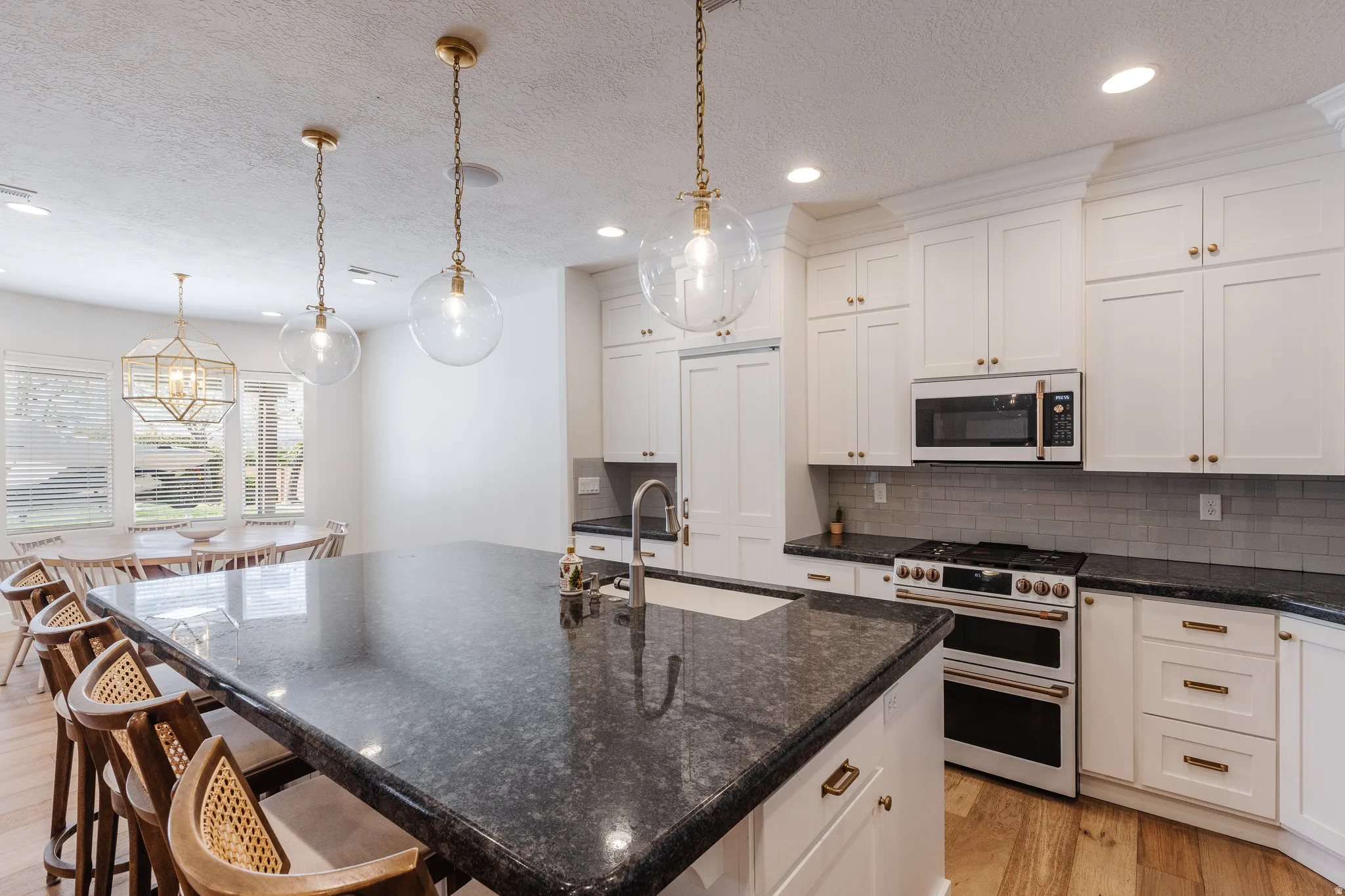 Kitchen featuring white appliances, light wood-style floors, dark stone countertops, a breakfast bar, and a textured ceiling