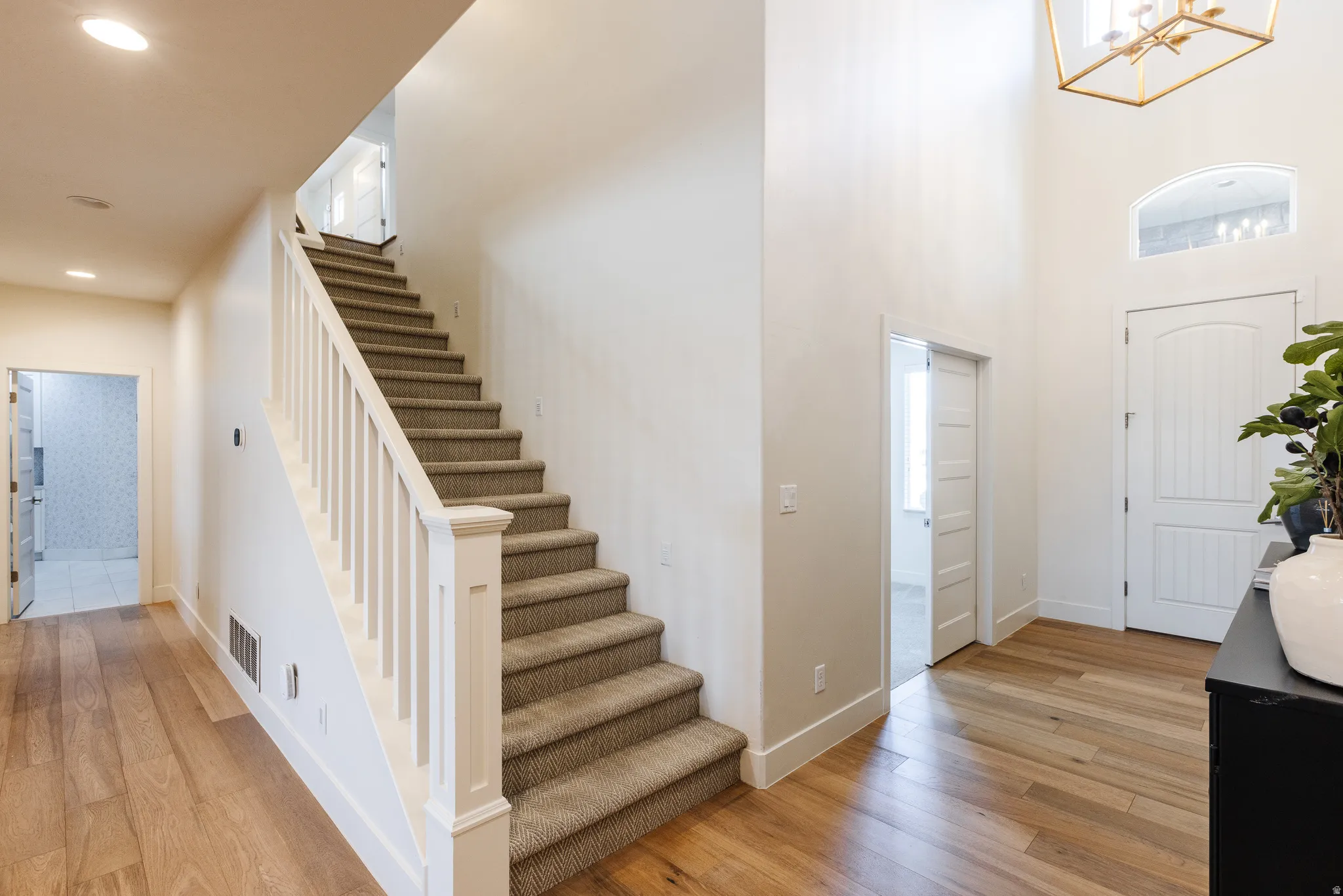 Entrance foyer featuring light wood-style flooring, suspended lighting, and a high ceiling