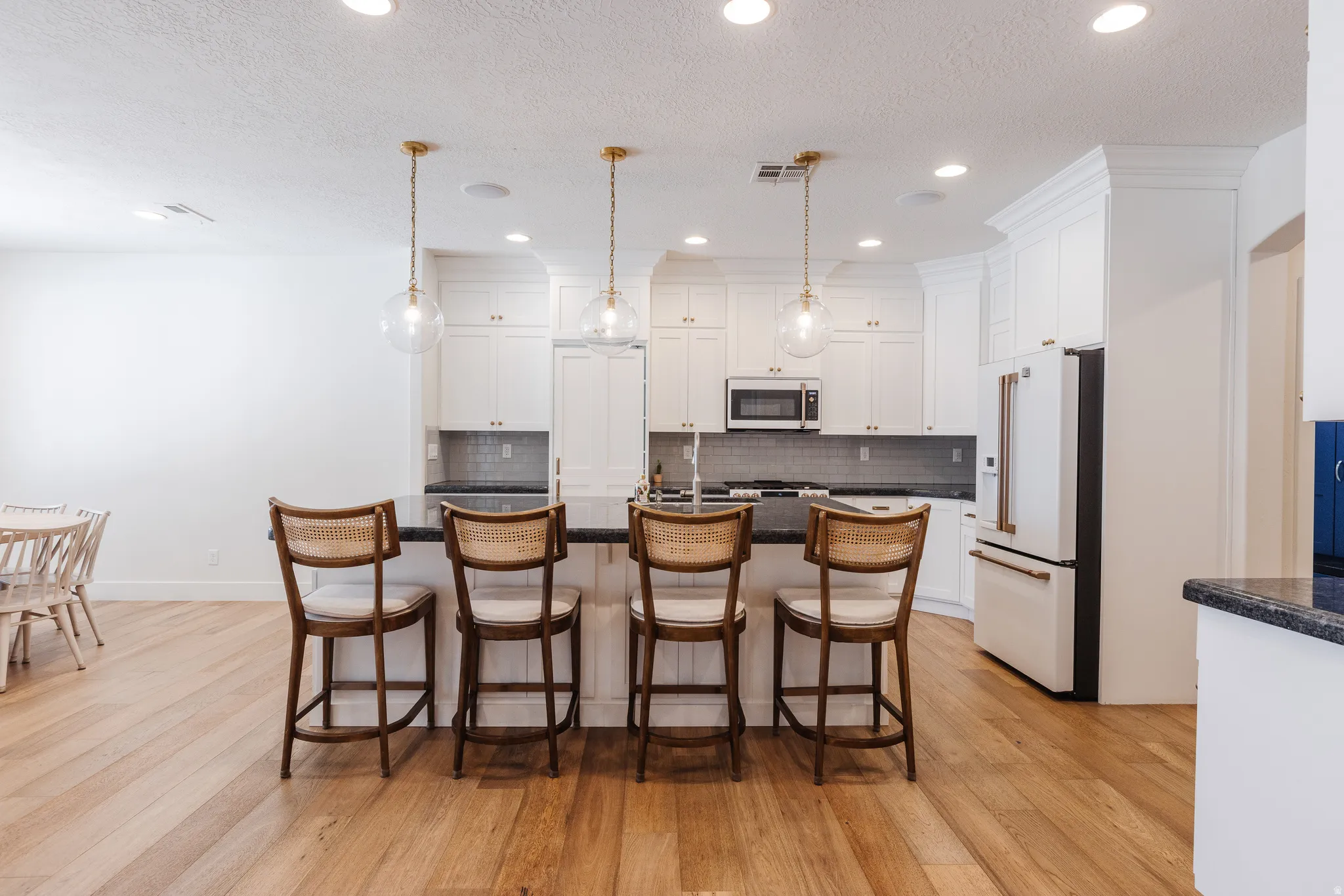 Kitchen with a center island with sink, high end white fridge, light wood-style floors, white cabinetry, and a textured ceiling