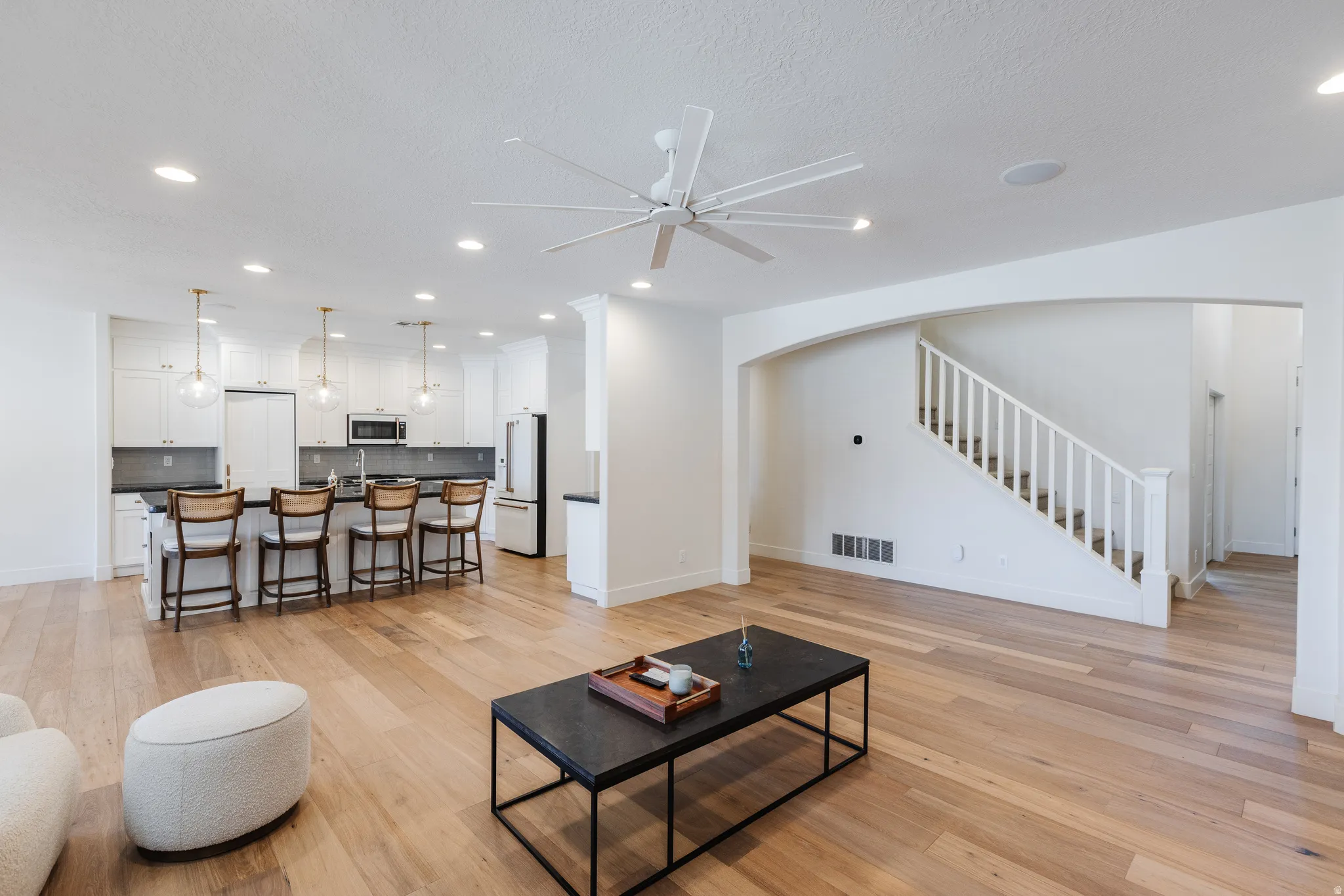 Living area with light wood-style flooring, arched walkways, recessed lighting, a ceiling fan, and a textured ceiling
