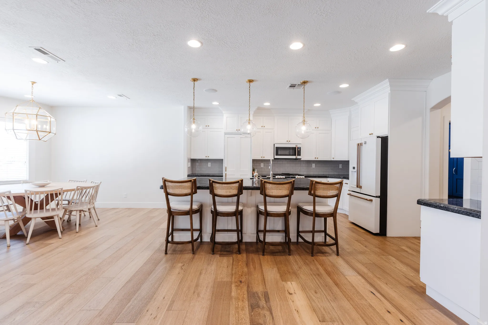 Kitchen featuring high end white fridge, a center island with sink, white cabinetry, light wood finished floors, and a kitchen bar