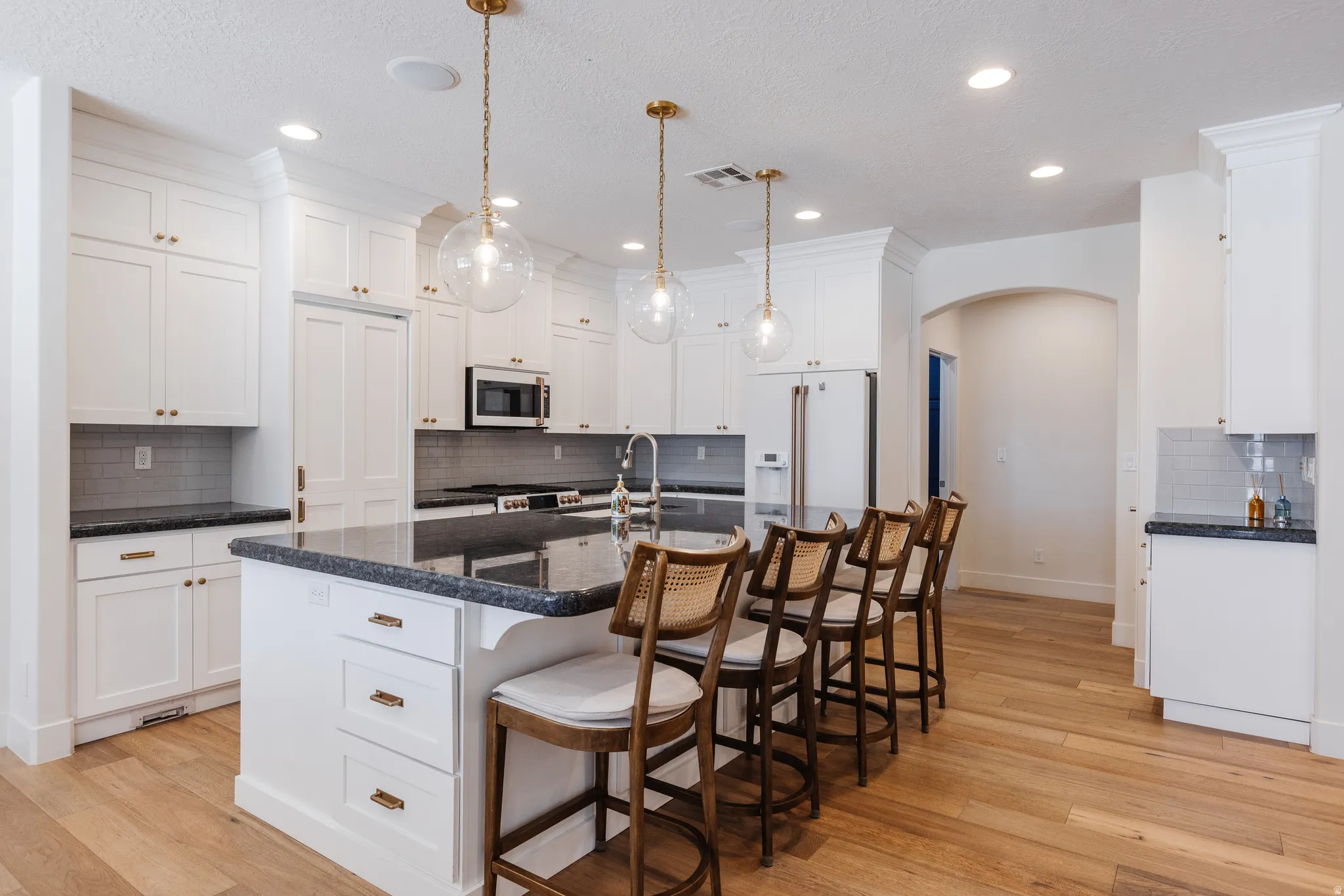Kitchen featuring arched walkways, a breakfast bar, decorative backsplash, an island with sink, and light wood-type flooring