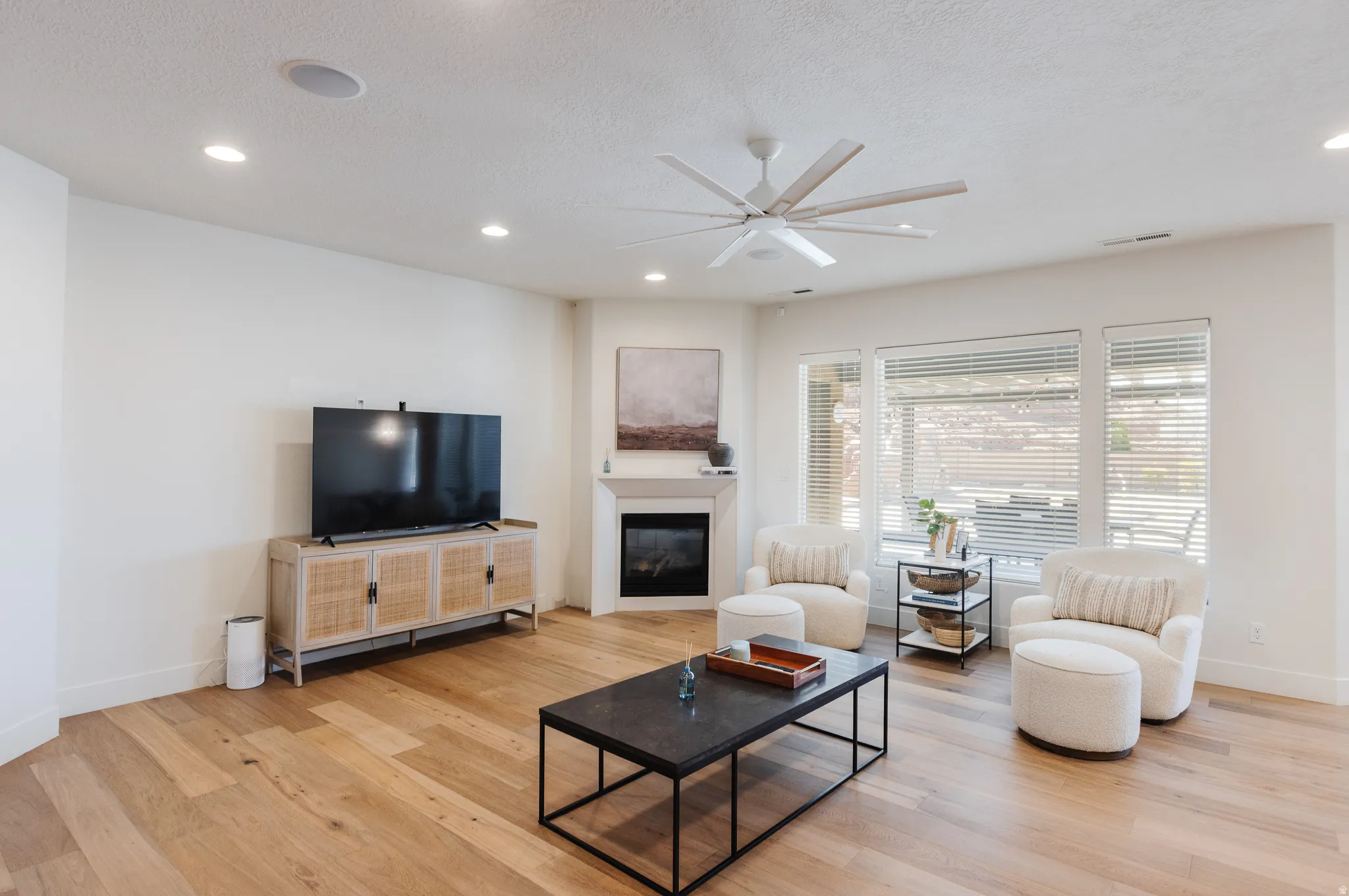 Living room with a glass covered fireplace, a ceiling fan, light wood finished floors, recessed lighting, and a textured ceiling