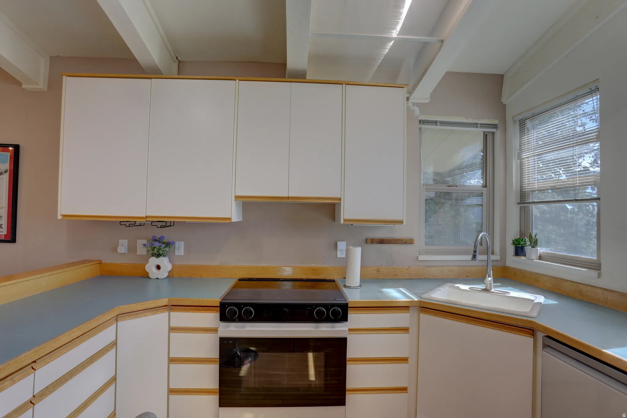 Kitchen featuring black range with electric cooktop, light countertops, stainless steel dishwasher, and two tone cabinetry