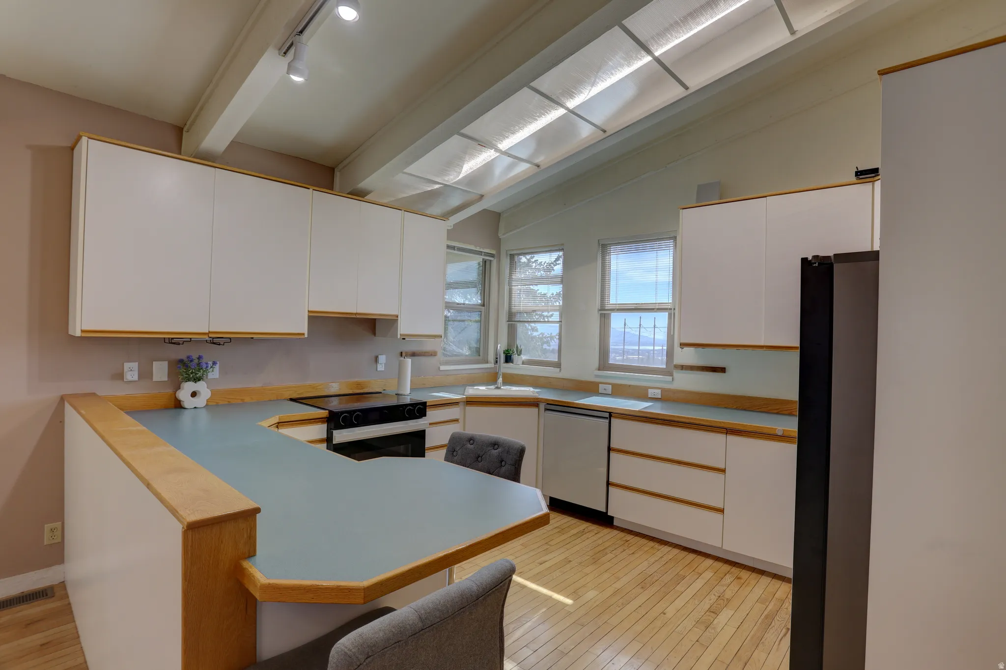 Dual tone kitchen featuring light wood-type flooring, black appliances, light countertops, a breakfast bar, and a peninsula