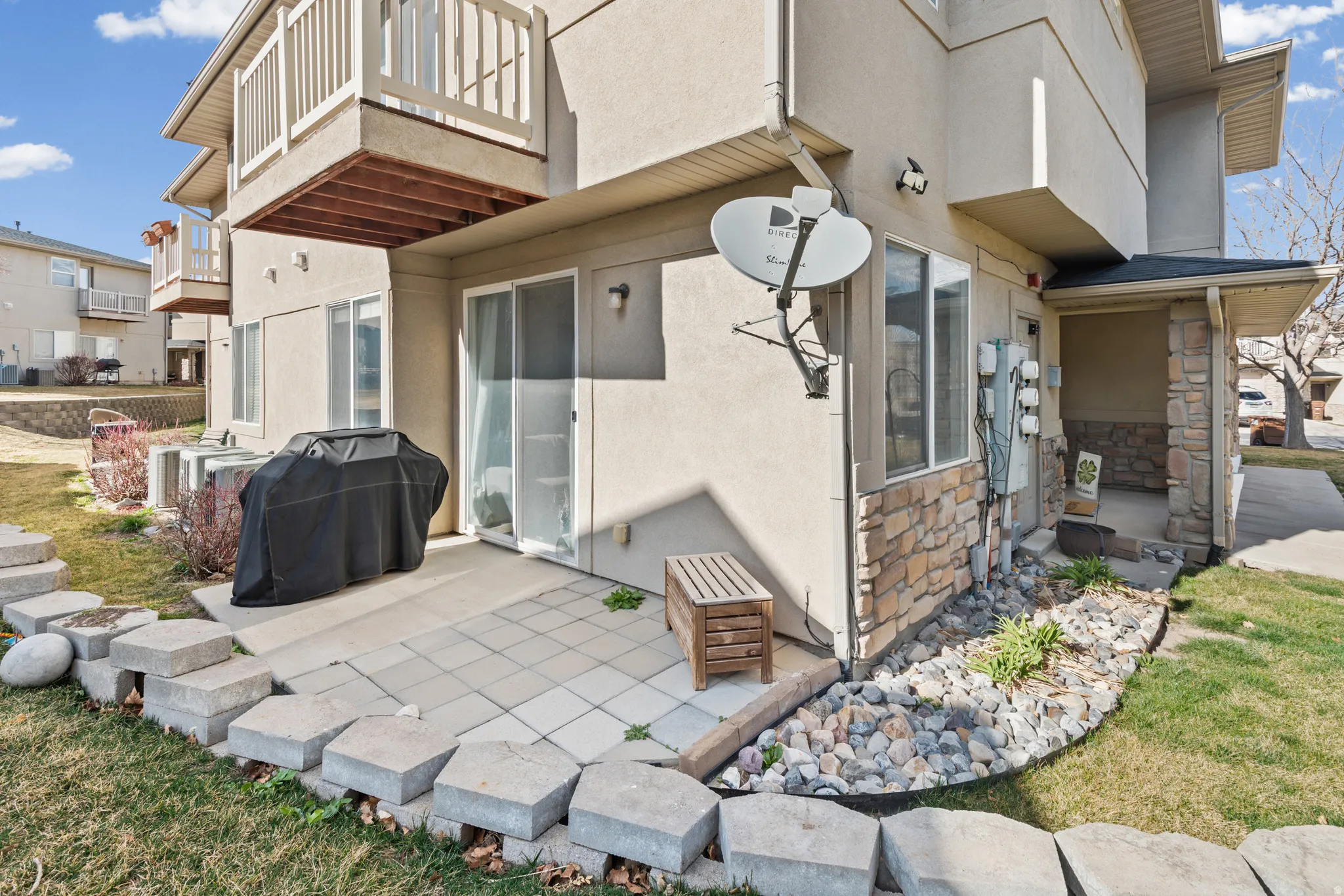 Back of property with stucco siding, stone siding, a balcony, and a patio area