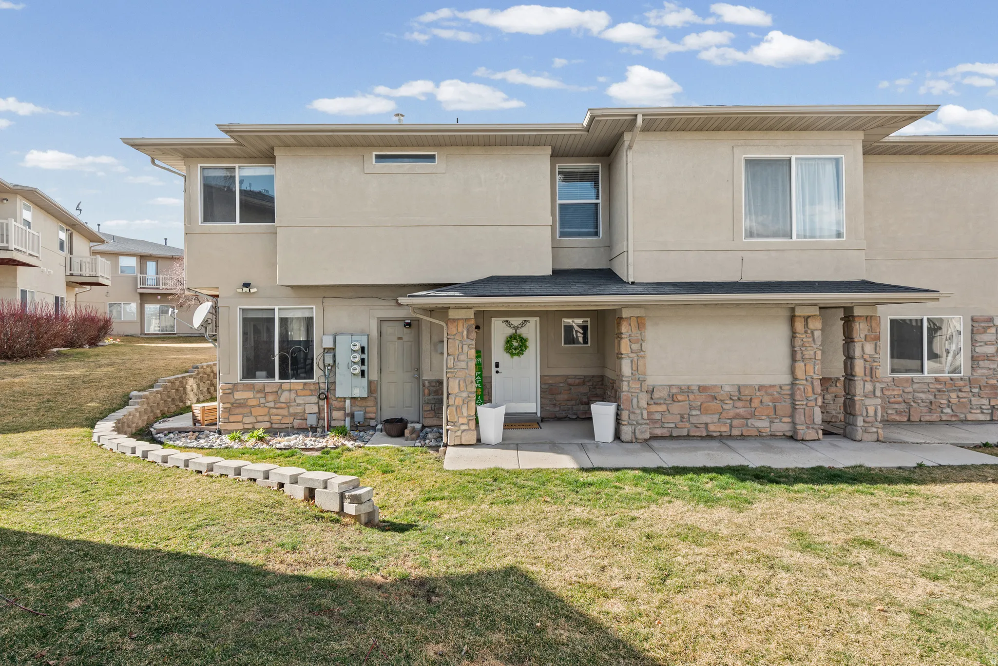 Rear view of property with a lawn, stucco siding, stone siding, and a porch