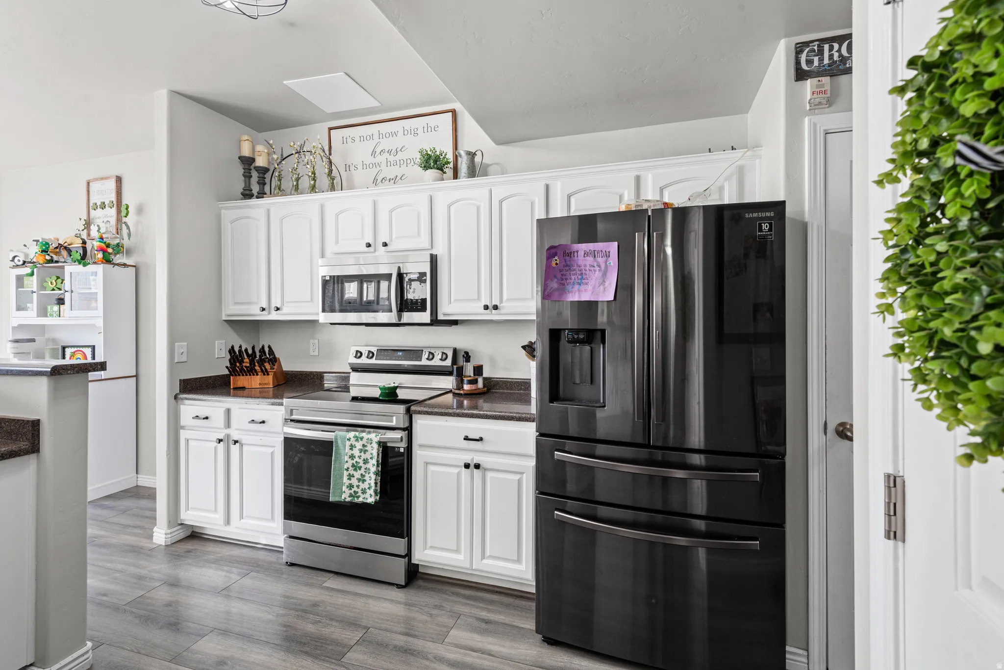 Kitchen with stainless steel appliances, white cabinets, dark wood finished floors, and dark stone countertops
