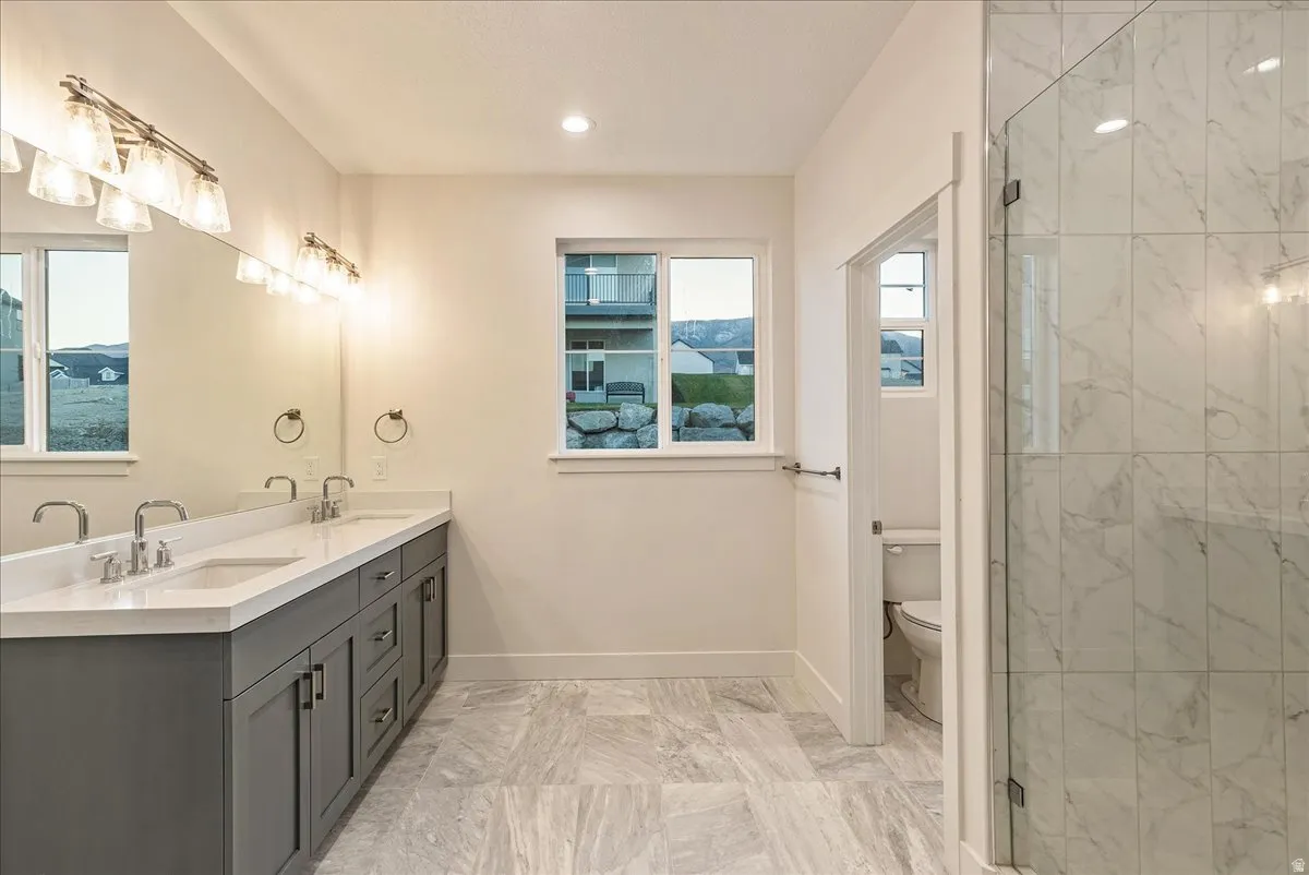 Primary bathroom featuring double vanity, a marble finish shower, light marble finish floors, and recessed lighting