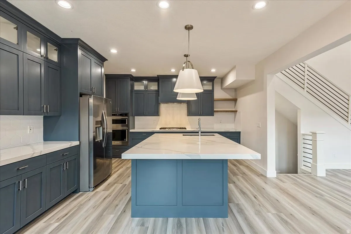 Kitchen with light stone counters, glass fronted cabinets, a kitchen island with sink, and light wood-type flooring