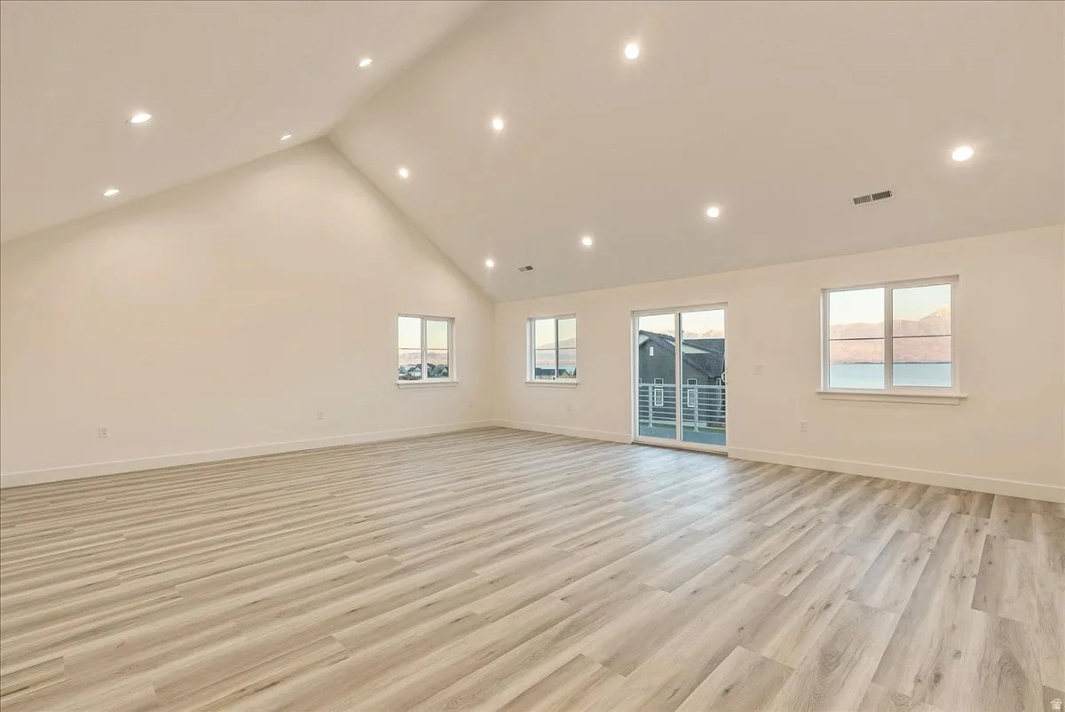 Empty room with a high ceiling, light wood finished floors, and recessed lighting