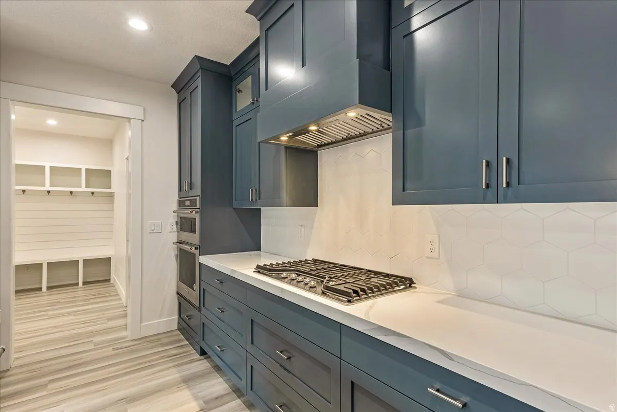 Kitchen with light wood finished floors, stainless steel appliances, recessed lighting, light stone countertops, and tasteful backsplash