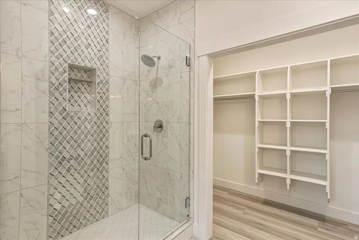 Primary bathroom featuring a shower stall, light wood-style floors, and a walk in closet
