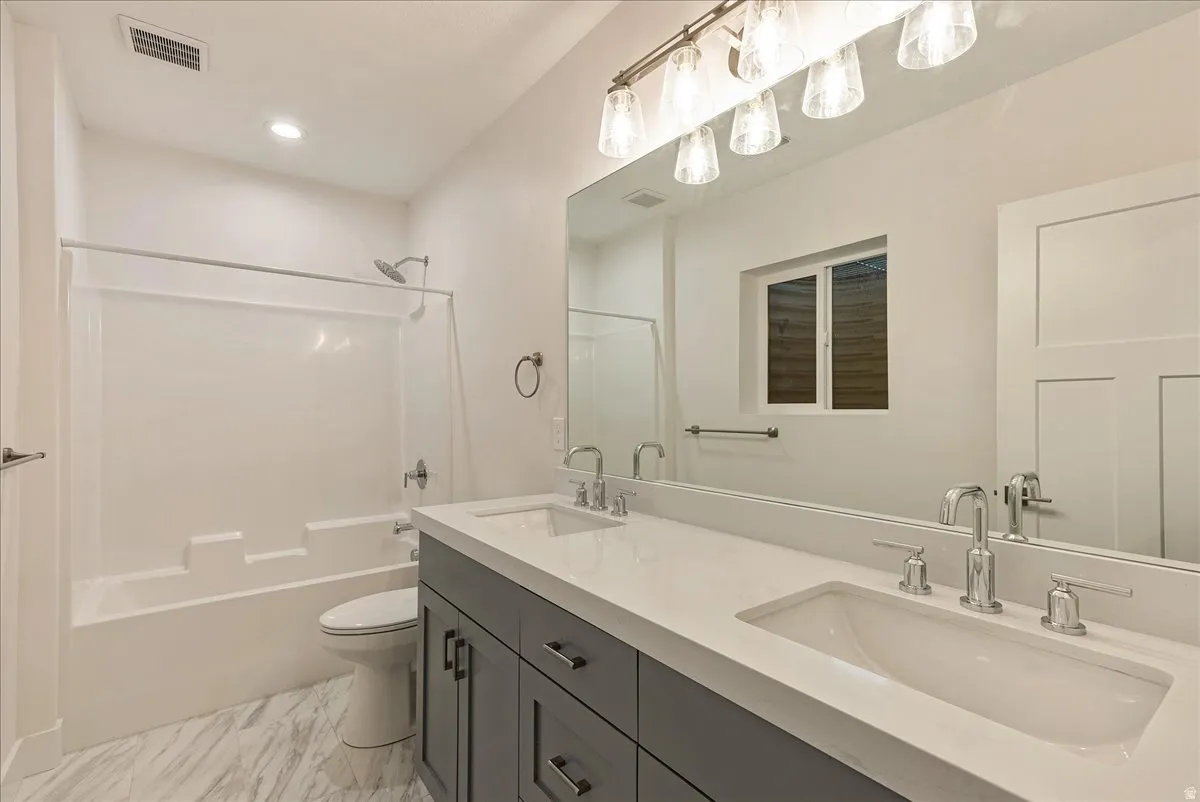Bathroom featuring double vanity, washtub / shower combination, and light marble finish floors