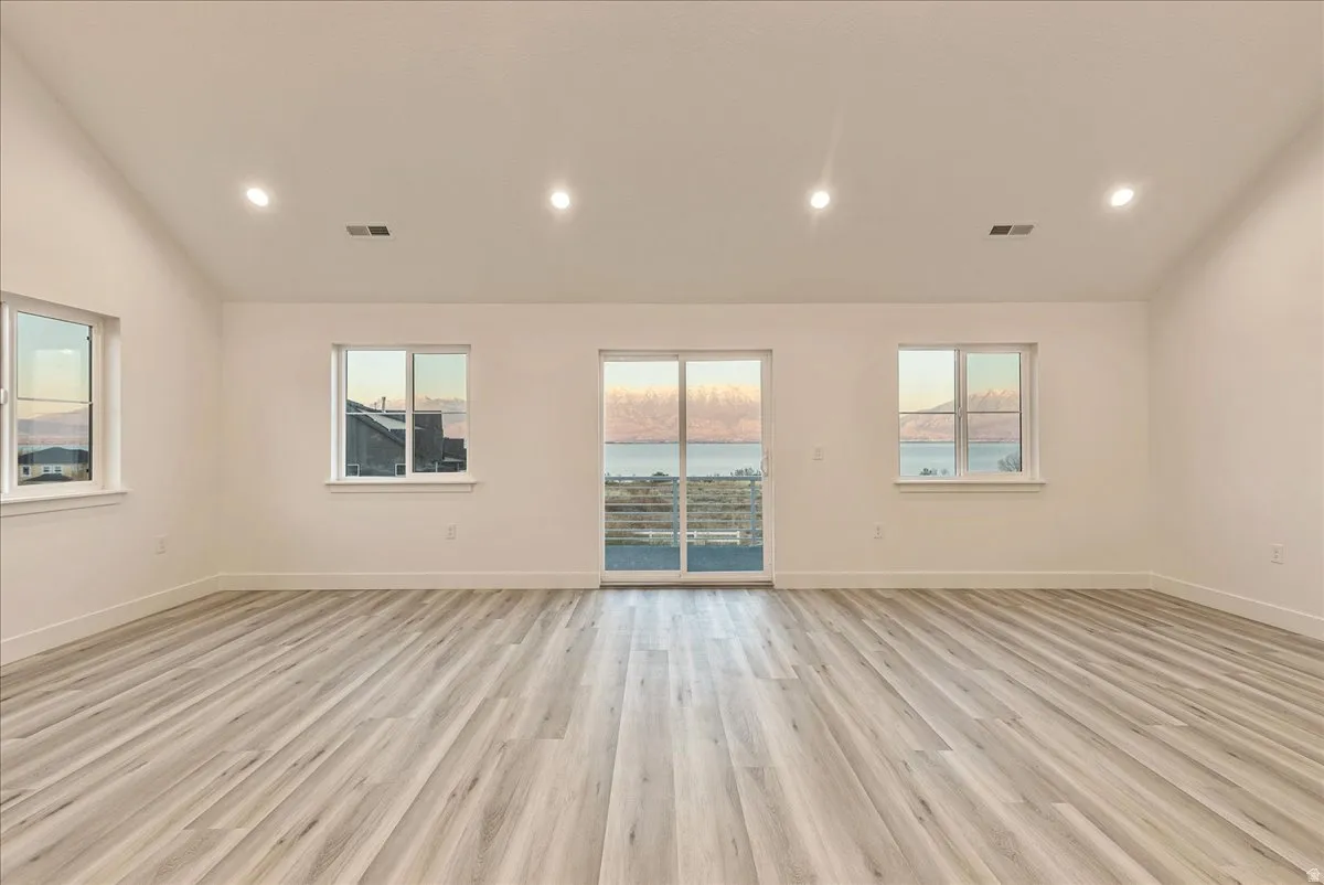 Unfurnished room with light wood finished floors, a water view, lofted ceiling, and recessed lighting