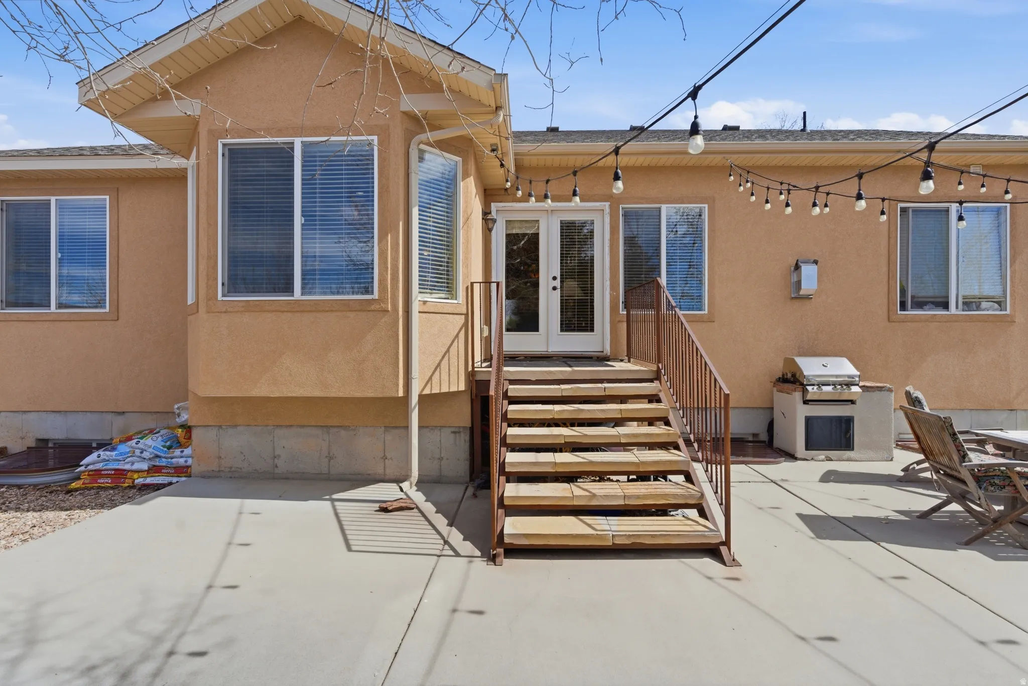 Rear exterior featuring a concrete patio, wood deck stairs with metal railings, and dual French doors