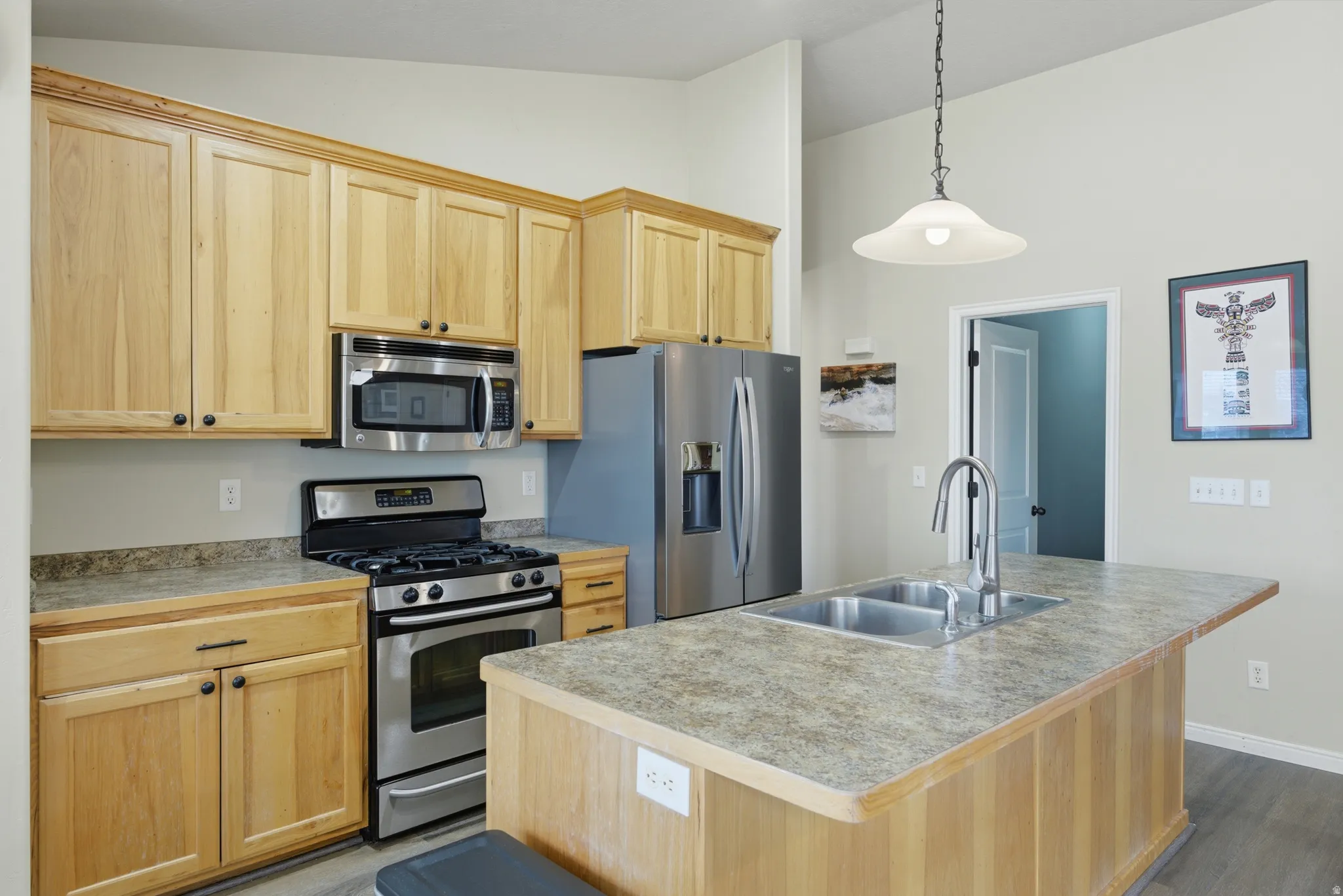 Kitchen featuring natural wood-finish cabinetry, stainless steel appliances, a center island with a double basin sink