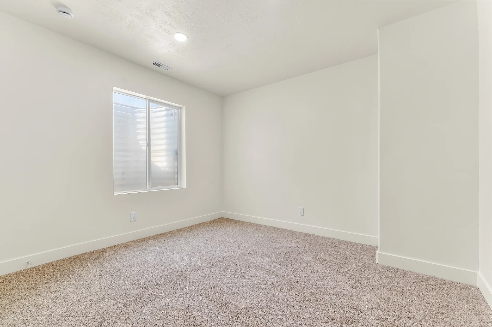 Empty room with light carpet, a smoke detector, and recessed lighting