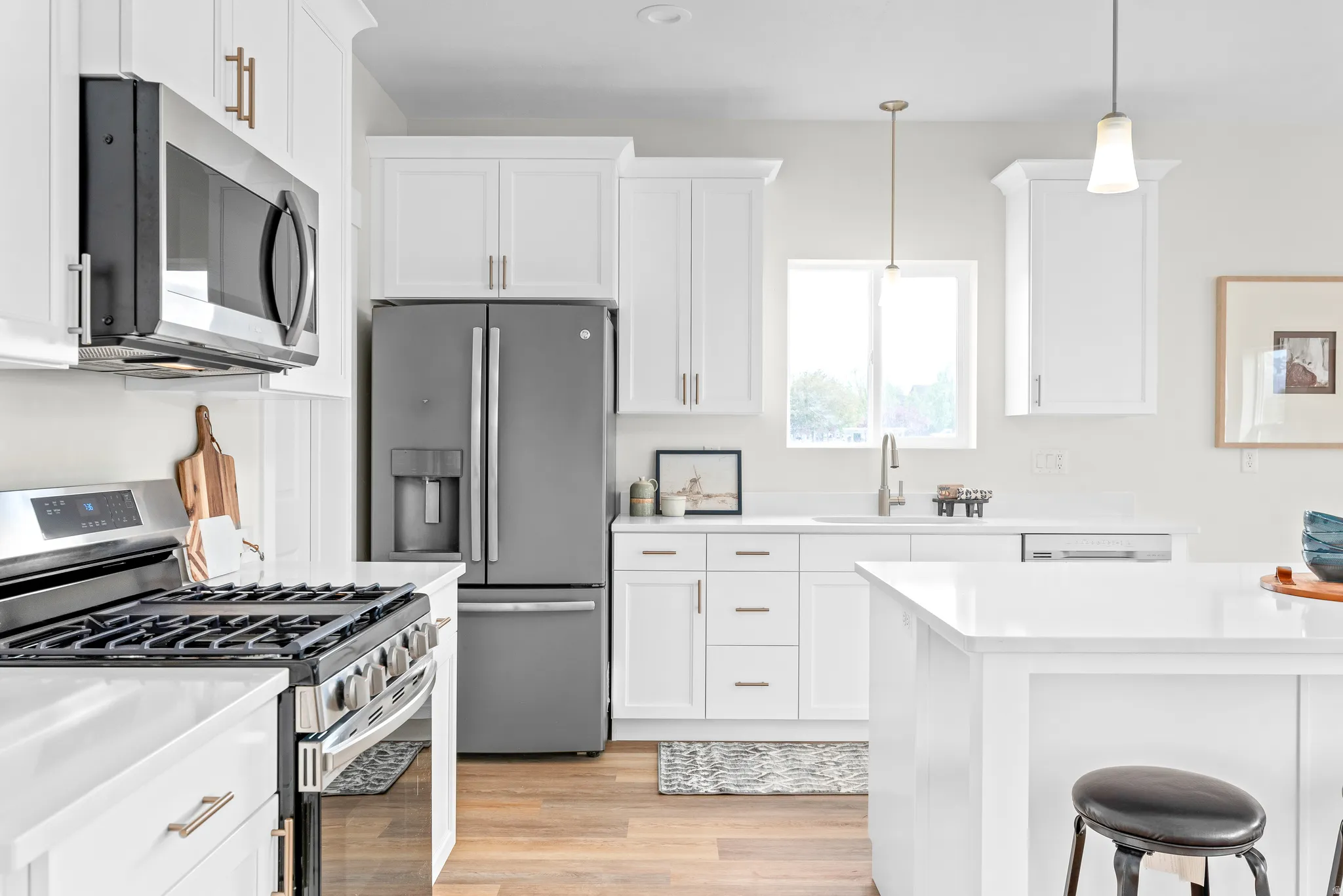 Kitchen featuring stainless steel appliances, white cabinets, decorative light fixtures, light wood-style flooring, and a kitchen breakfast bar