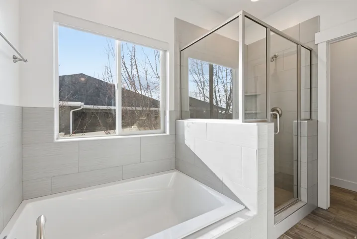 Full bath featuring a stall shower, a bath, and wood finished floors