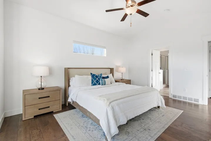 Bedroom with dark wood finished floors, lofted ceiling, ceiling fan, and ensuite bathroom