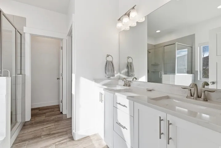 Full bath with double vanity, a stall shower, and light wood-style floors
