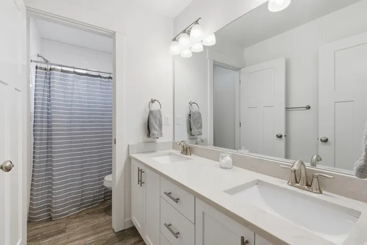 Bathroom with double vanity, a shower with shower curtain, and dark wood-style flooring
