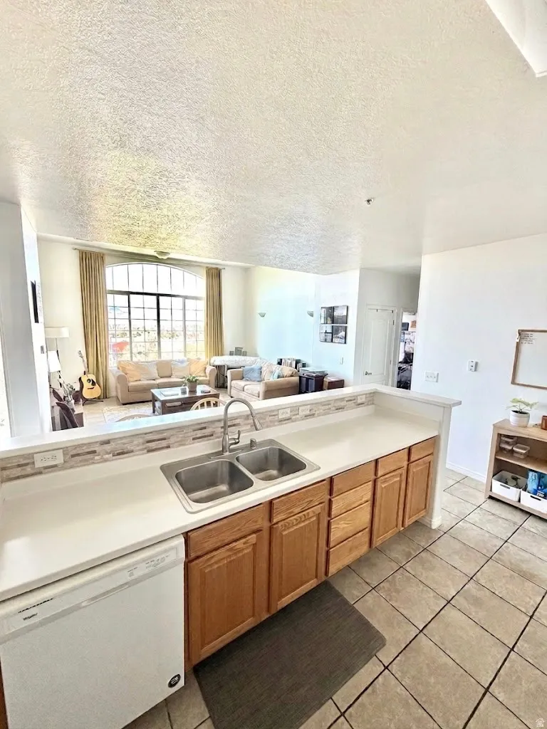 Kitchen with open floor plan, light countertops, dishwasher, a textured ceiling, and light tile patterned flooring