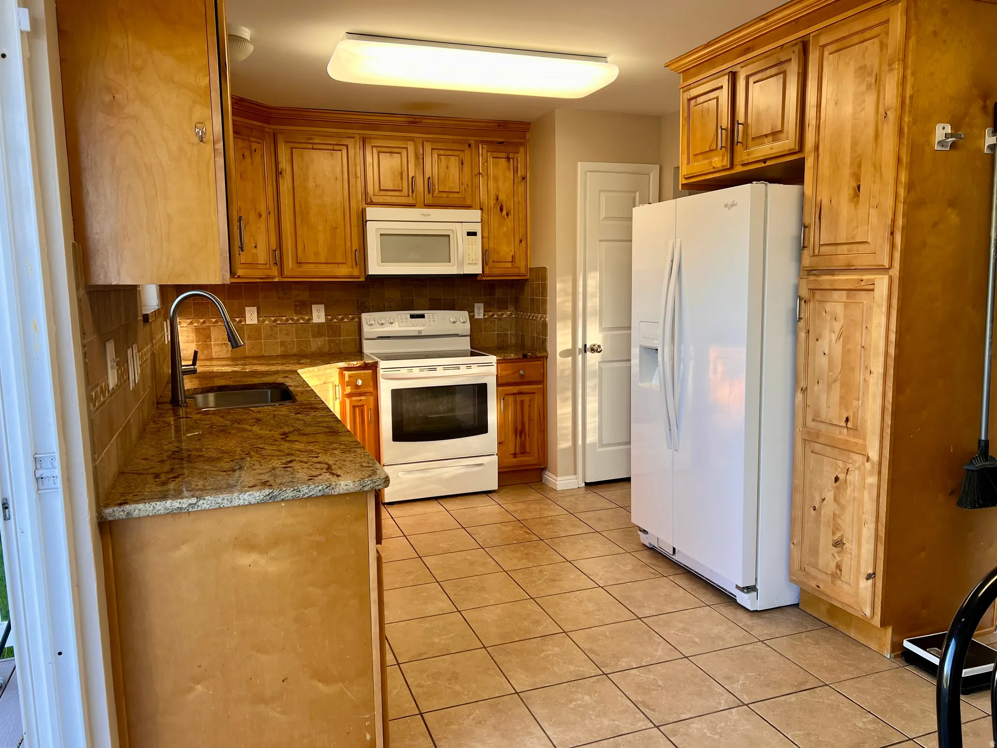 Kitchen featuring wood finish cabinetry, white appliances, tasteful backsplash, and light tile patterned floors