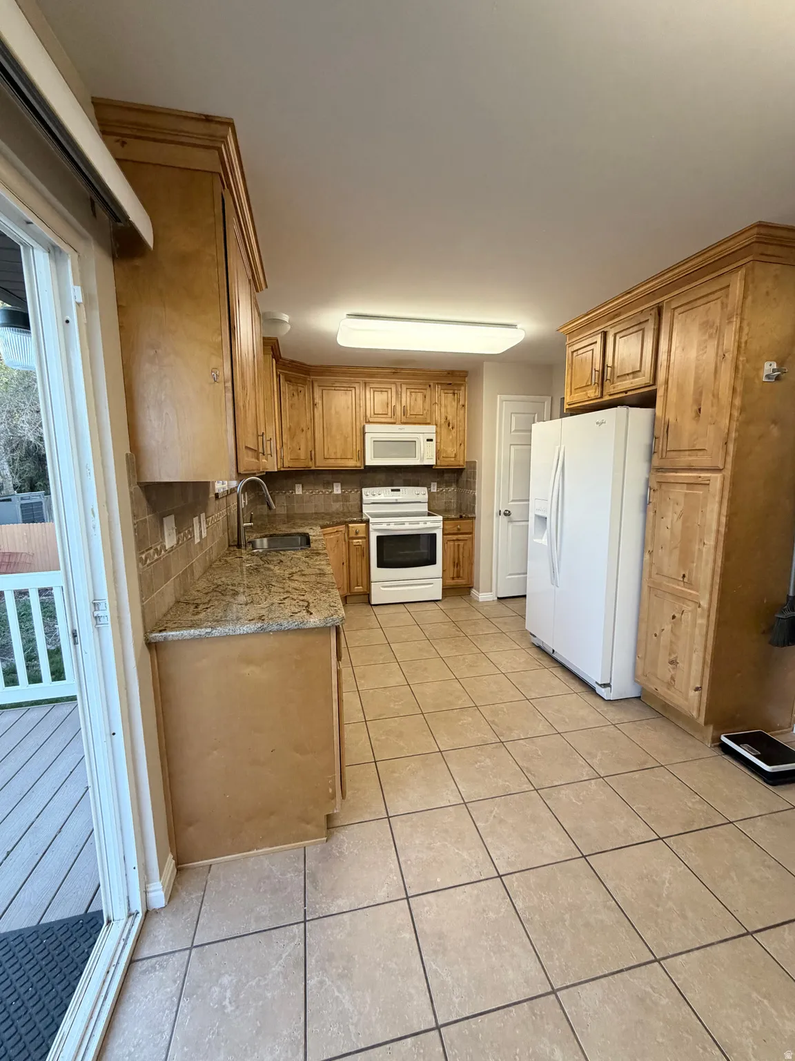 Kitchen with tasteful backsplash, white appliances, light stone countertops, and light tile patterned floors