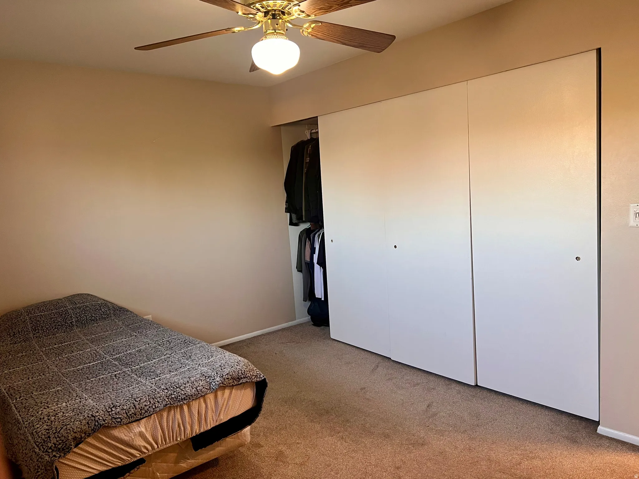 Bedroom with light colored carpet, a closet, and a ceiling fan