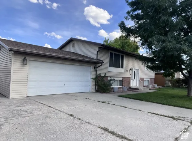 Split-level residence featuring light-toned siding, an attached two-car garage, white entry door with side lights, and a manicured lawn
