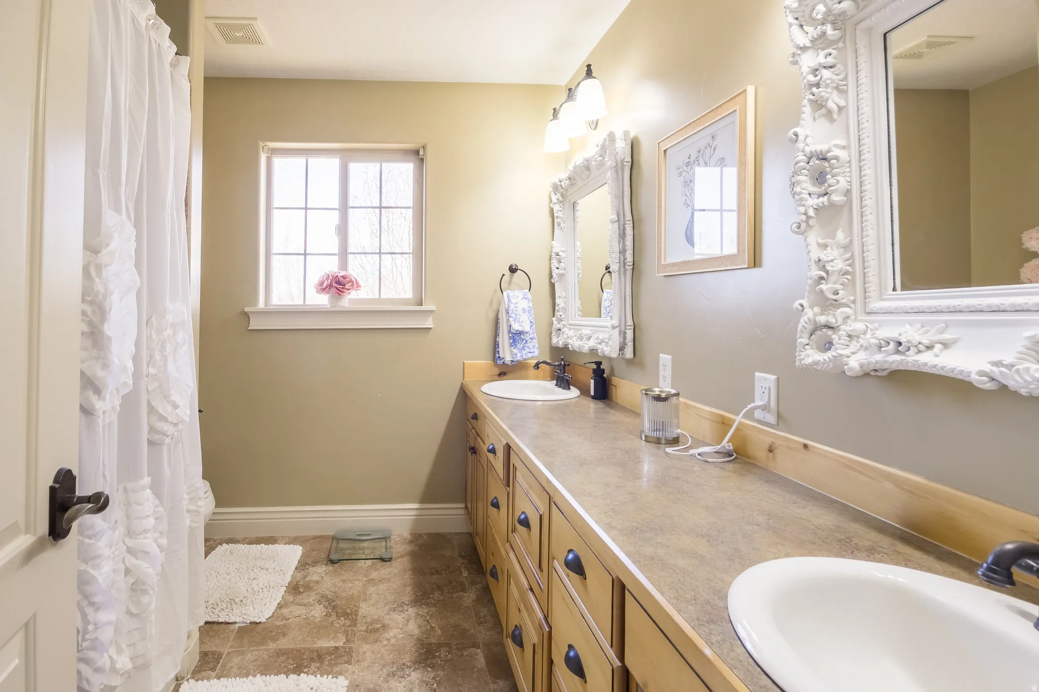 Full bath with double vanity, a shower with shower curtain, and dark stone finish floors