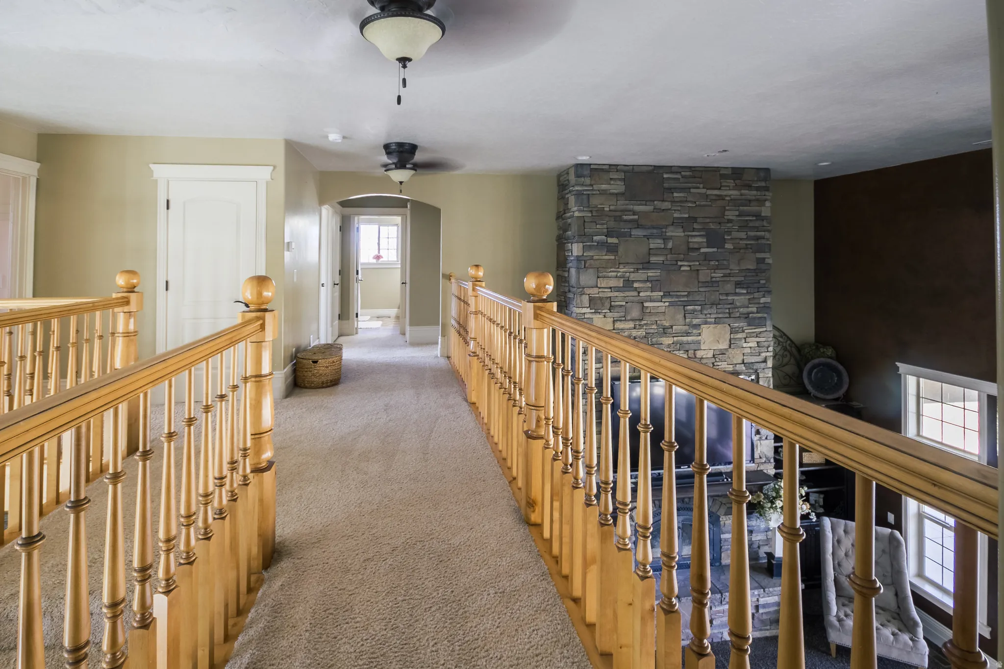 Hallway with an upstairs landing, carpet flooring, and arched walkways