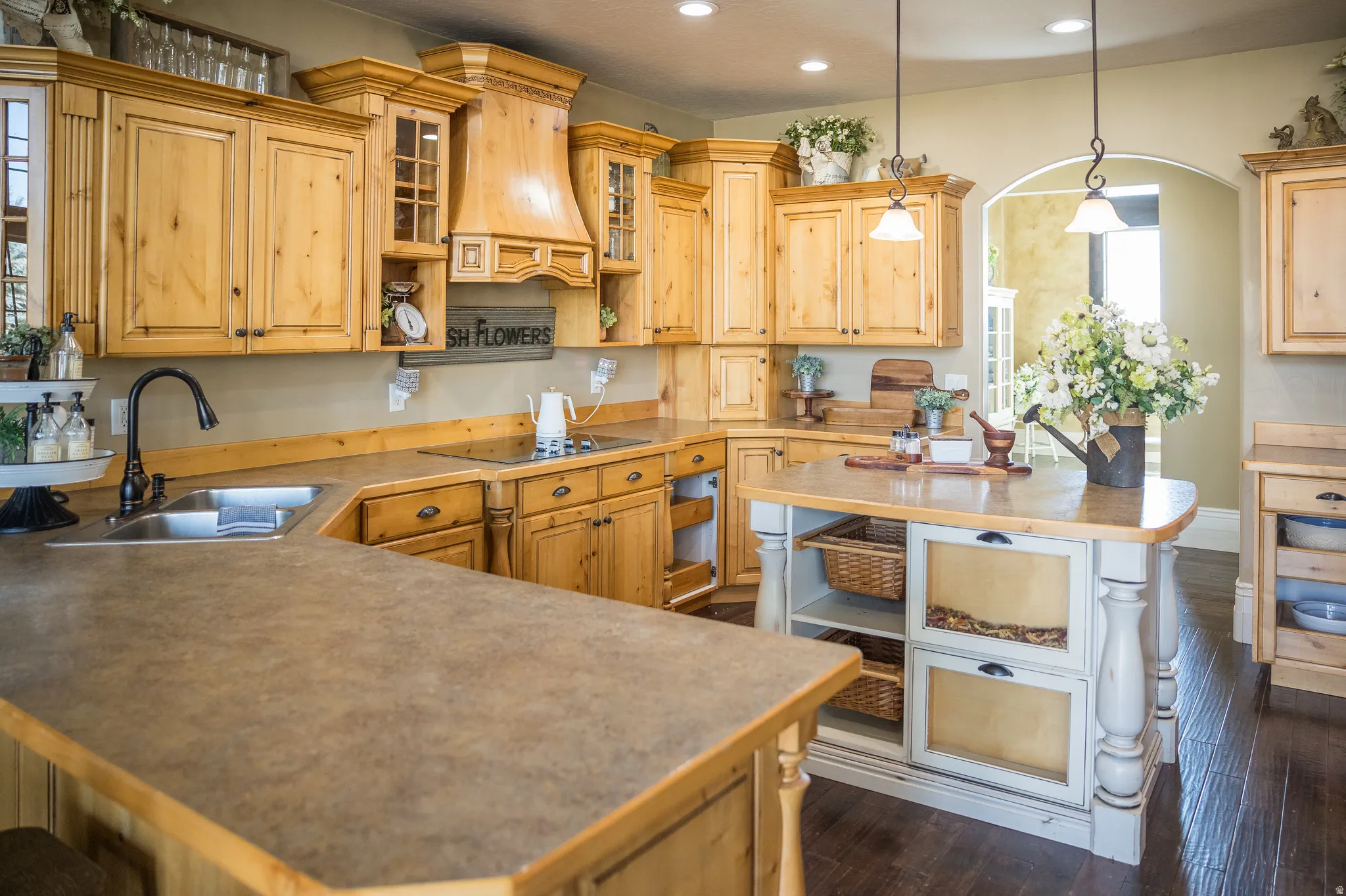 Kitchen with open shelves, glass insert cabinets, pendant lighting, dark wood finished floors, and a peninsula