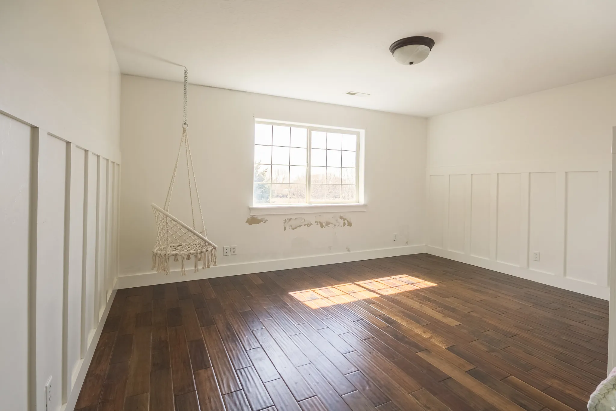 Unfurnished room with a decorative wall, dark wood-style flooring, and a wainscoted wall