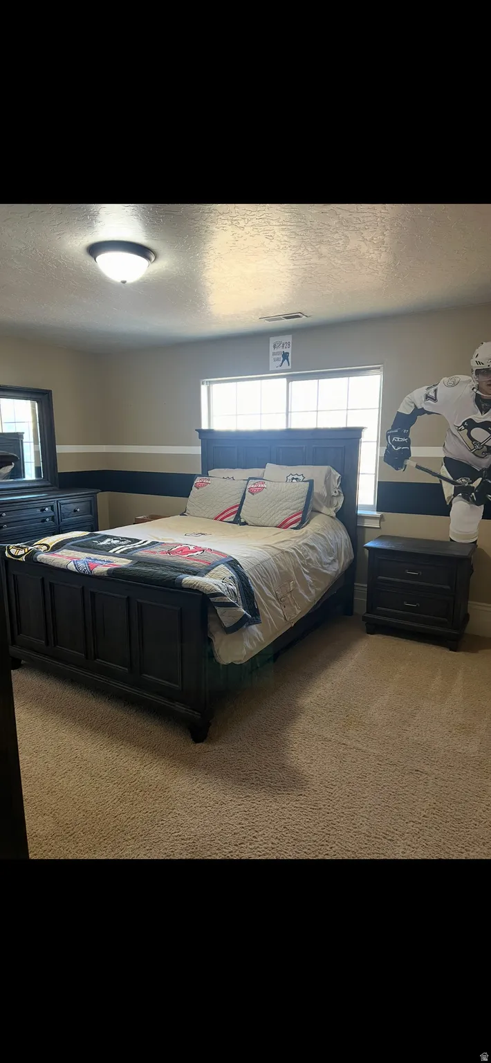 Bedroom featuring light colored carpet, multiple windows, and a textured ceiling