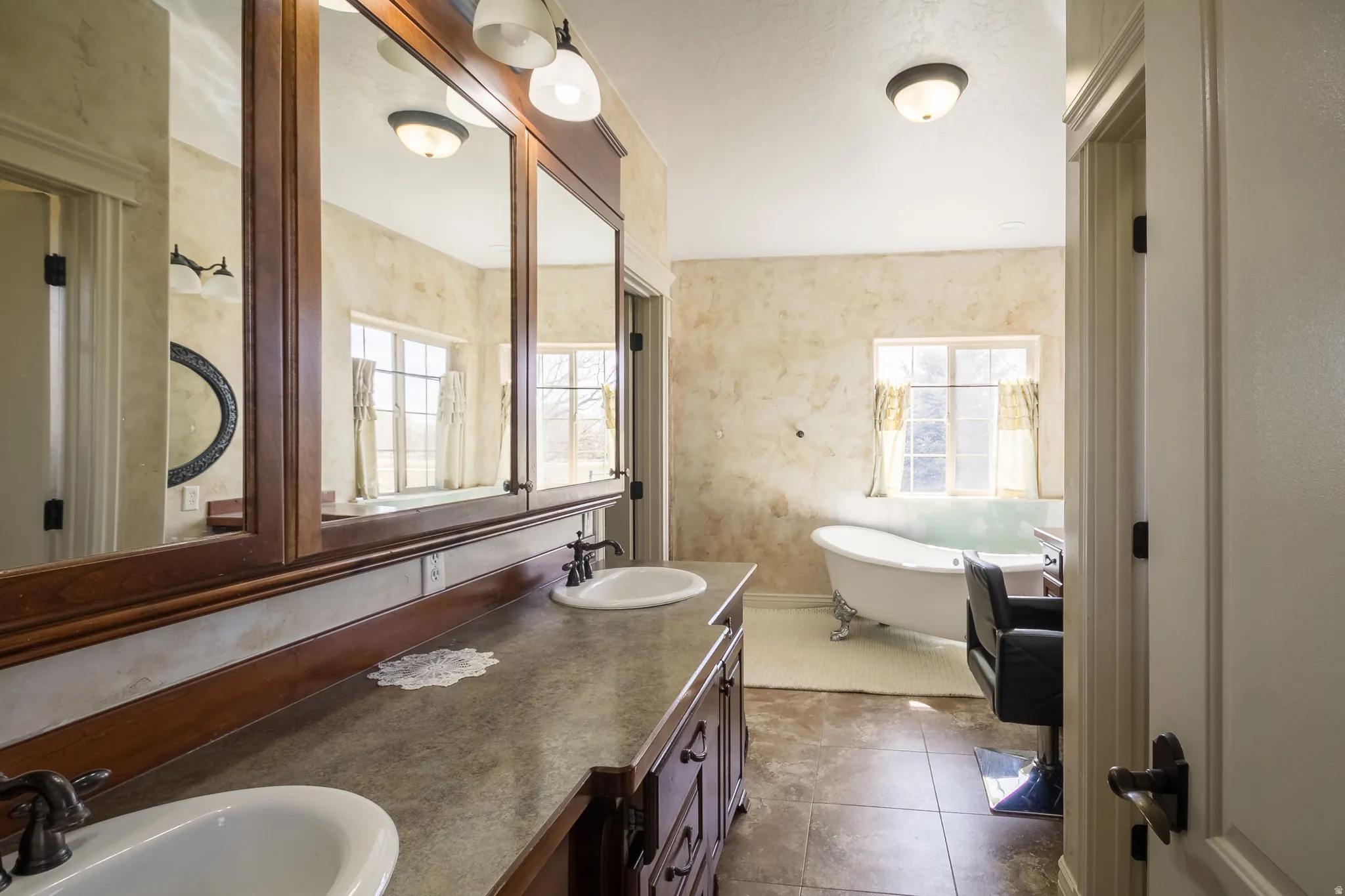 Bathroom featuring double vanity, a freestanding tub, and dark tile patterned flooring