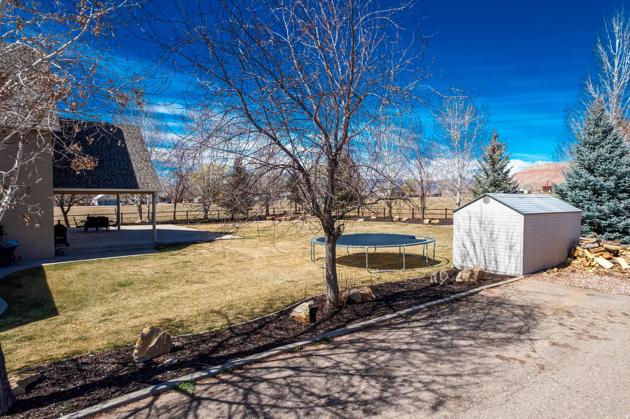 Fenced backyard with a storage unit, a trampoline, and a patio area