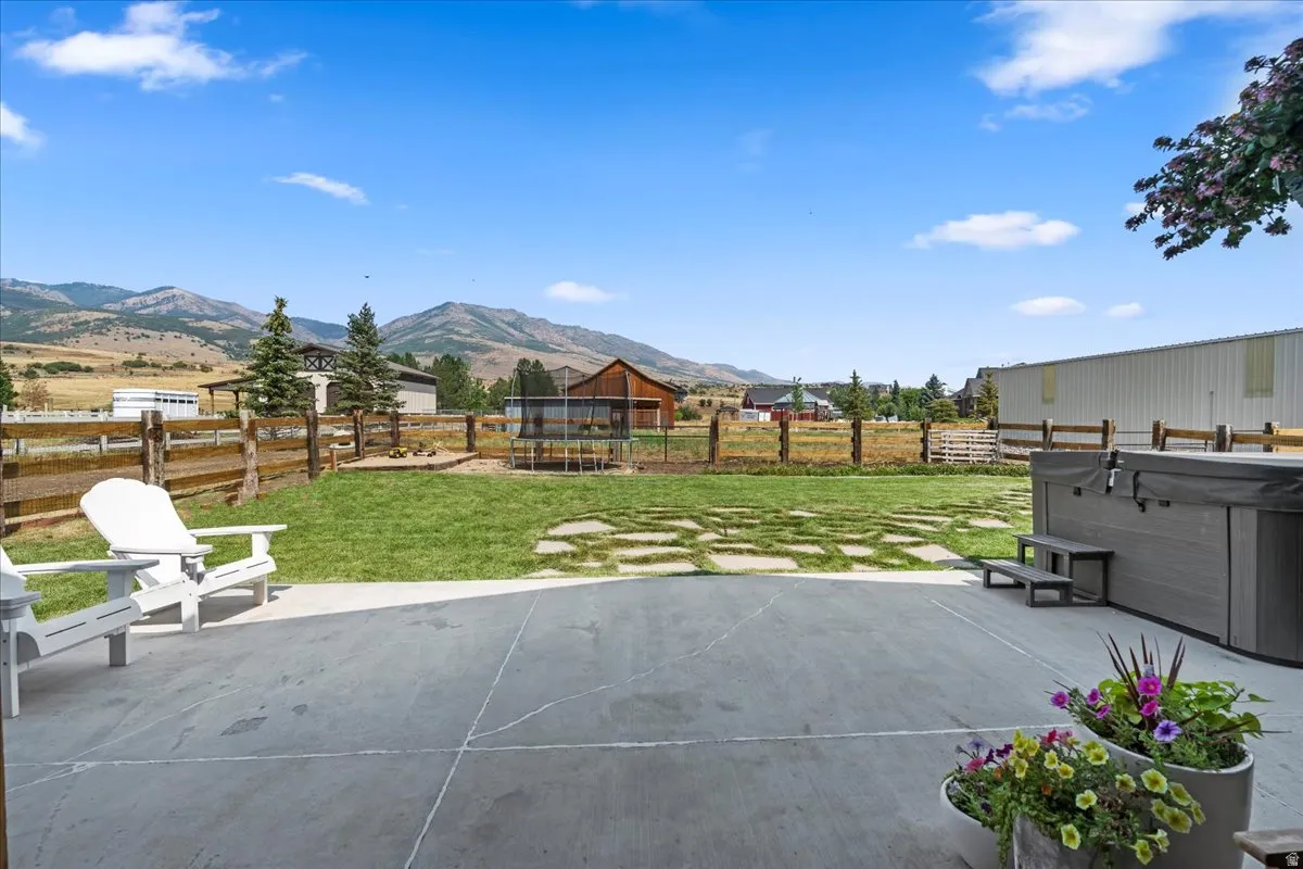 Fenced backyard featuring a trampoline, a patio area, a mountain view, and a hot tub